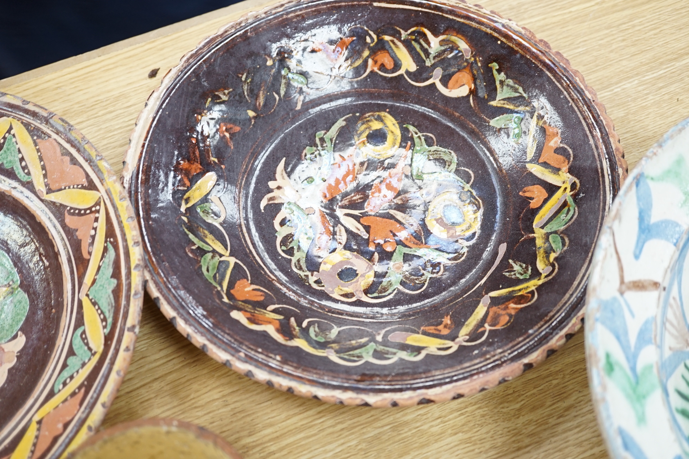 A group of Mediterranean slipware dishes, bowls and jugs, decorated in colours on a predominantly brown or ochre ground, the largest 33cm in diameter